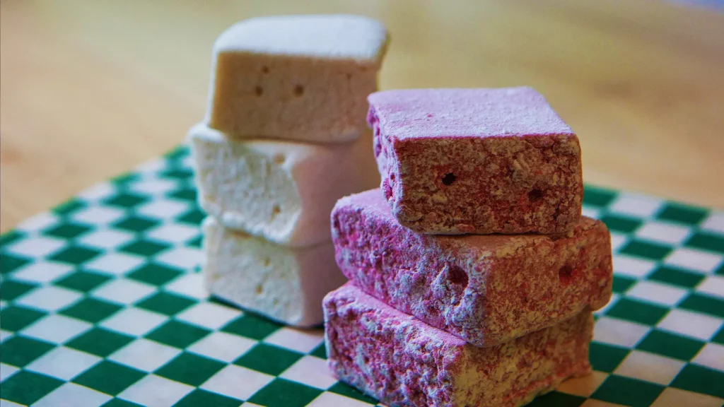 Two stacks of square marshmallows on a green and white checkered board. The vibrant purple marshmallows are made with farm-grown haskap berries from Strom's Farm and Bakery in Guelph, Ontario, giving them a sweet and tart flavor that tastes like a mix of blueberries, raspberries, and blackberries.