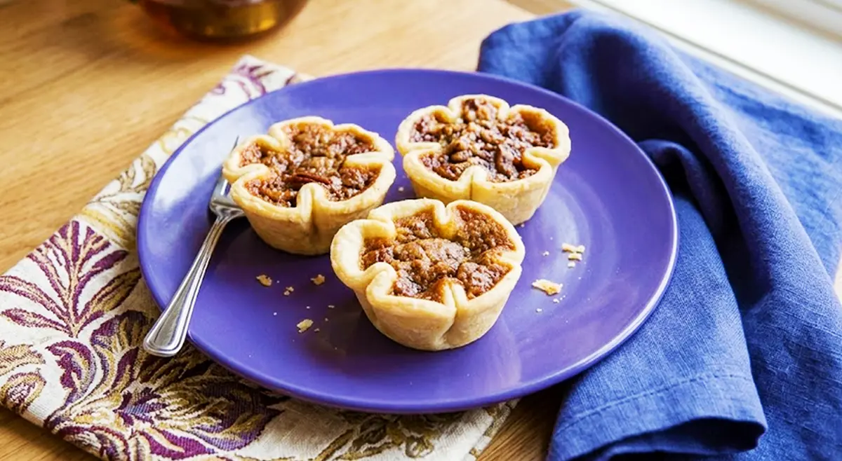 Three of our signature flower-shaped pecan butter tarts served on a purple plate at Strom's Farm & Bakery in Guelph, Ontario. These homemade tarts feature a thick filling made with pure butter and absolutely no corn syrup.
