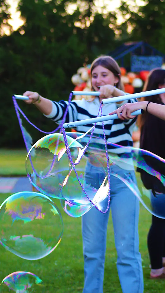 Young adults enjoying the outdoor play activities blowing up soap-balloons during the Weekday Harvest Fun Adventure at Strom's Farm in Guelph, surrounded by bright autumn foliage.